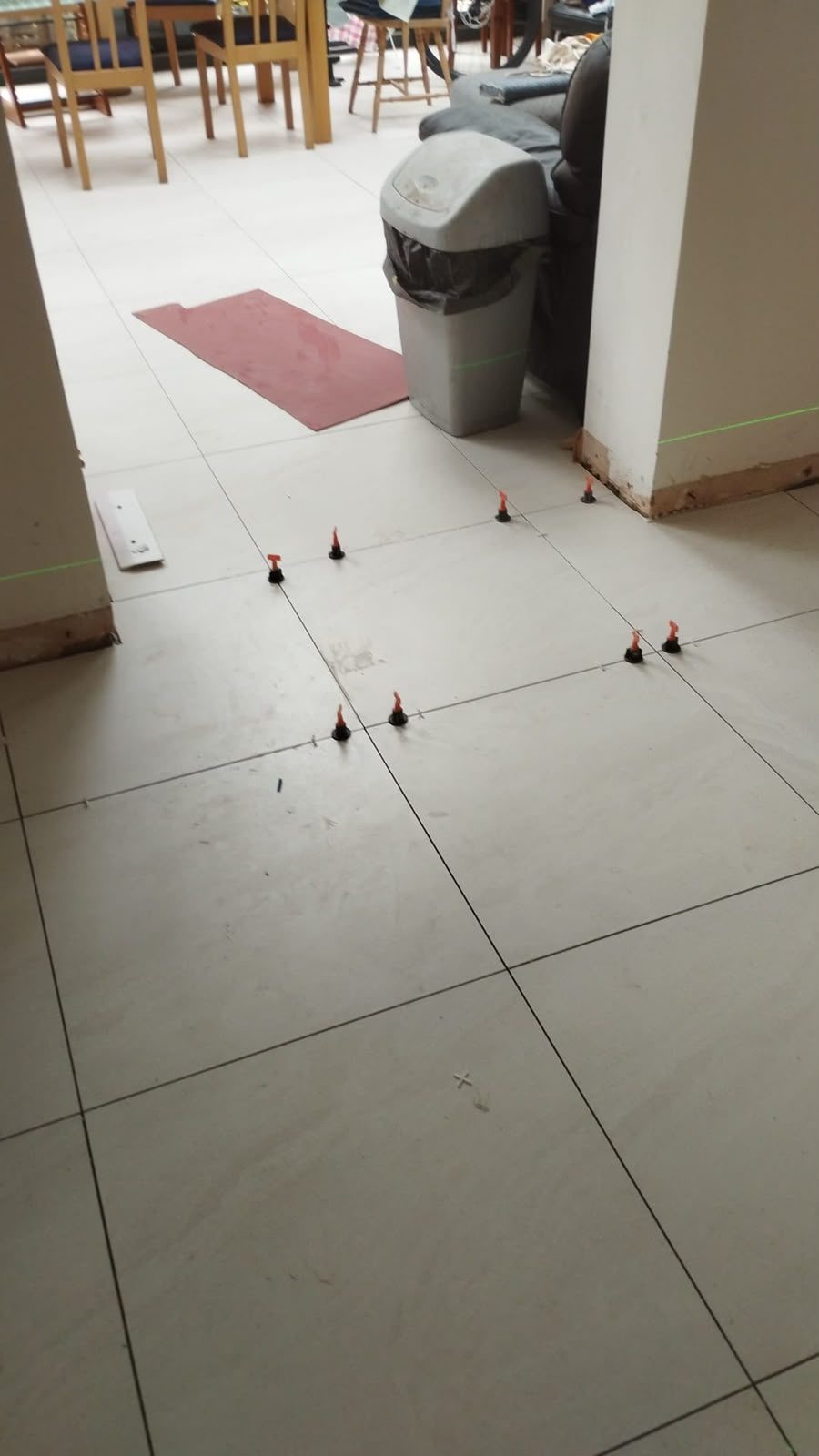 Large-format porcelain floor tiles being laid with a levelling clip system and a laser guide line across a room.