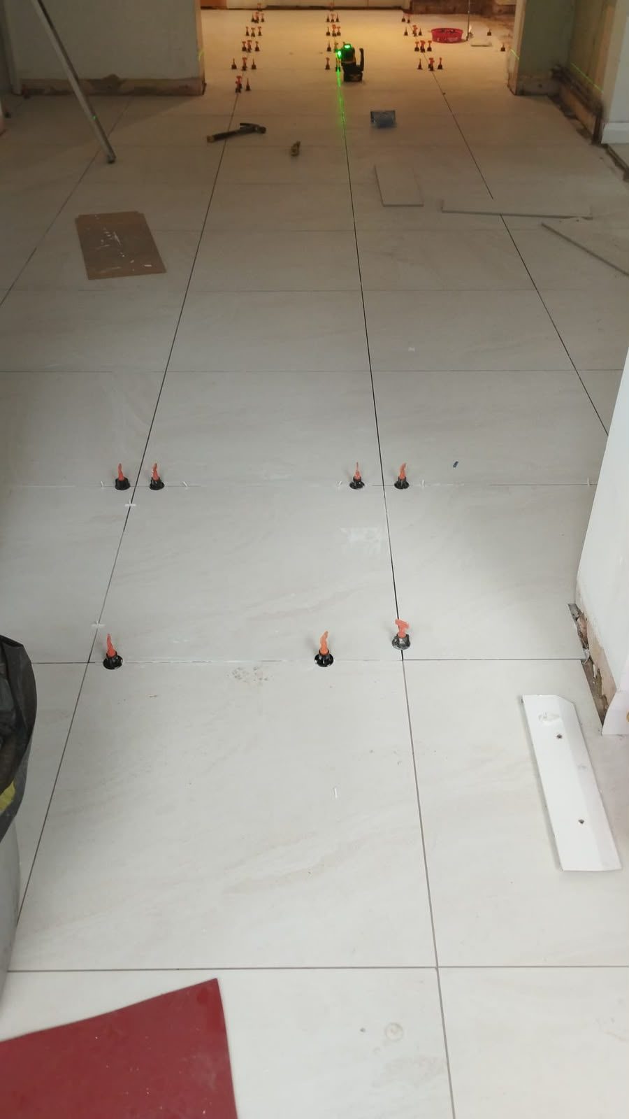 An open-plan floor being tiled, set out with a laser line and levelling clips mid-installation.