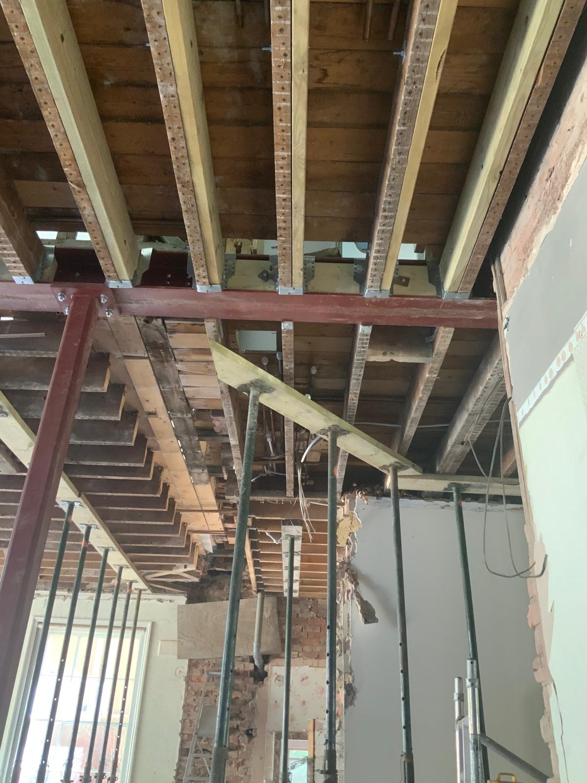 Exposed ceiling showing wooden beams, metal supports, and partially demolished walls during a building refurbishment.
