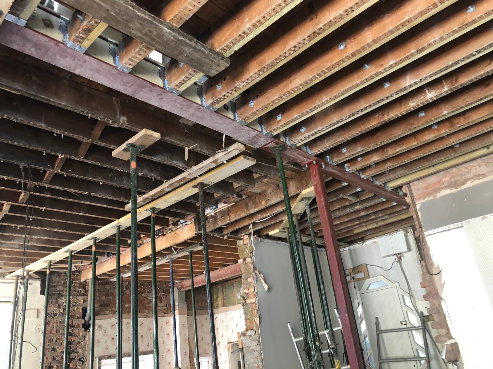 Exposed ceiling joists and steel beam supported by temporary props in a partially demolished room under refurbishment.