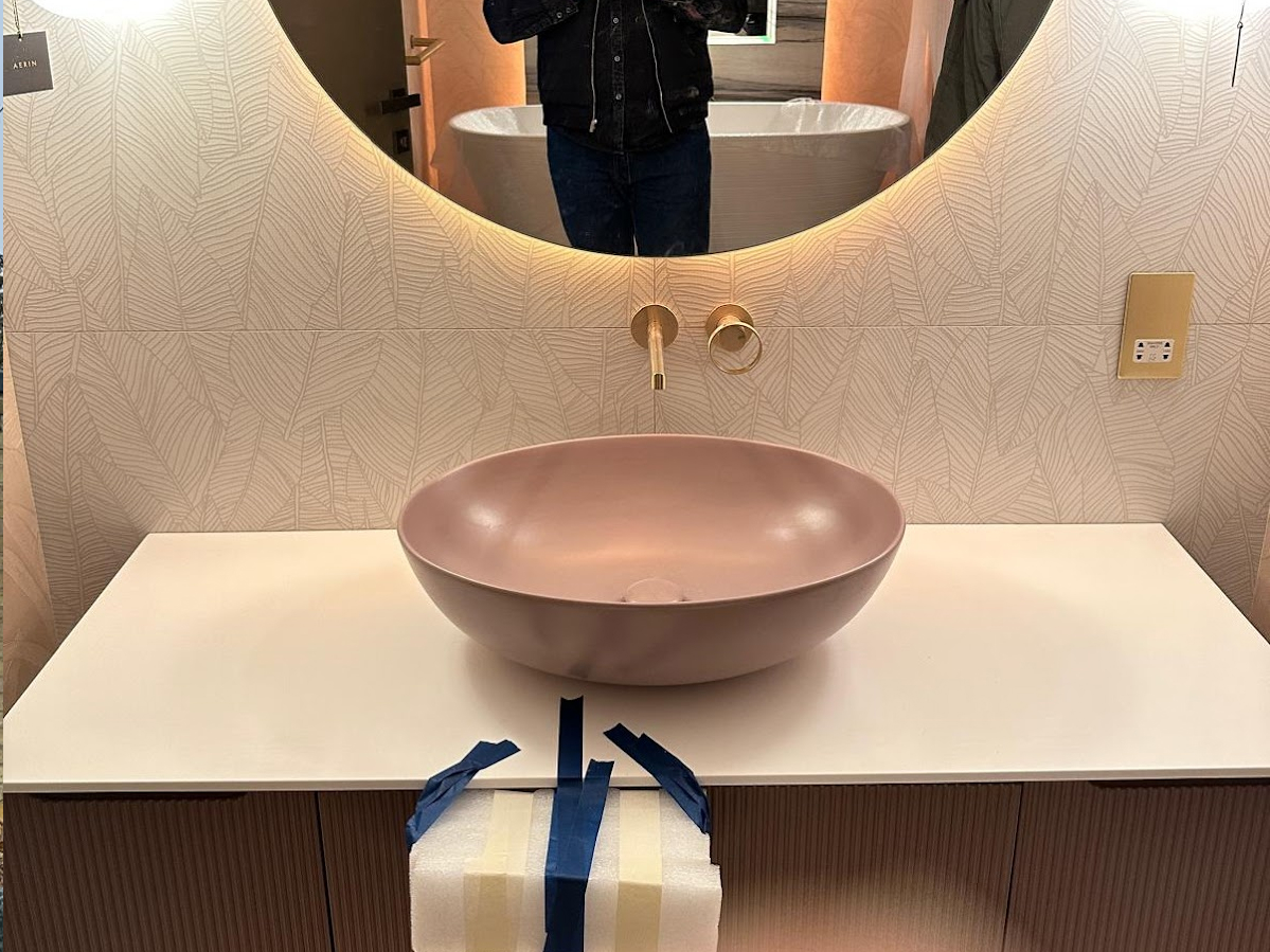 A modern bathroom vanity with a round pink basin, wall-mounted tap, large round mirror, and paper towels taped to the worktop—perfectly complementing homes after a Sash Window Repair South London project.