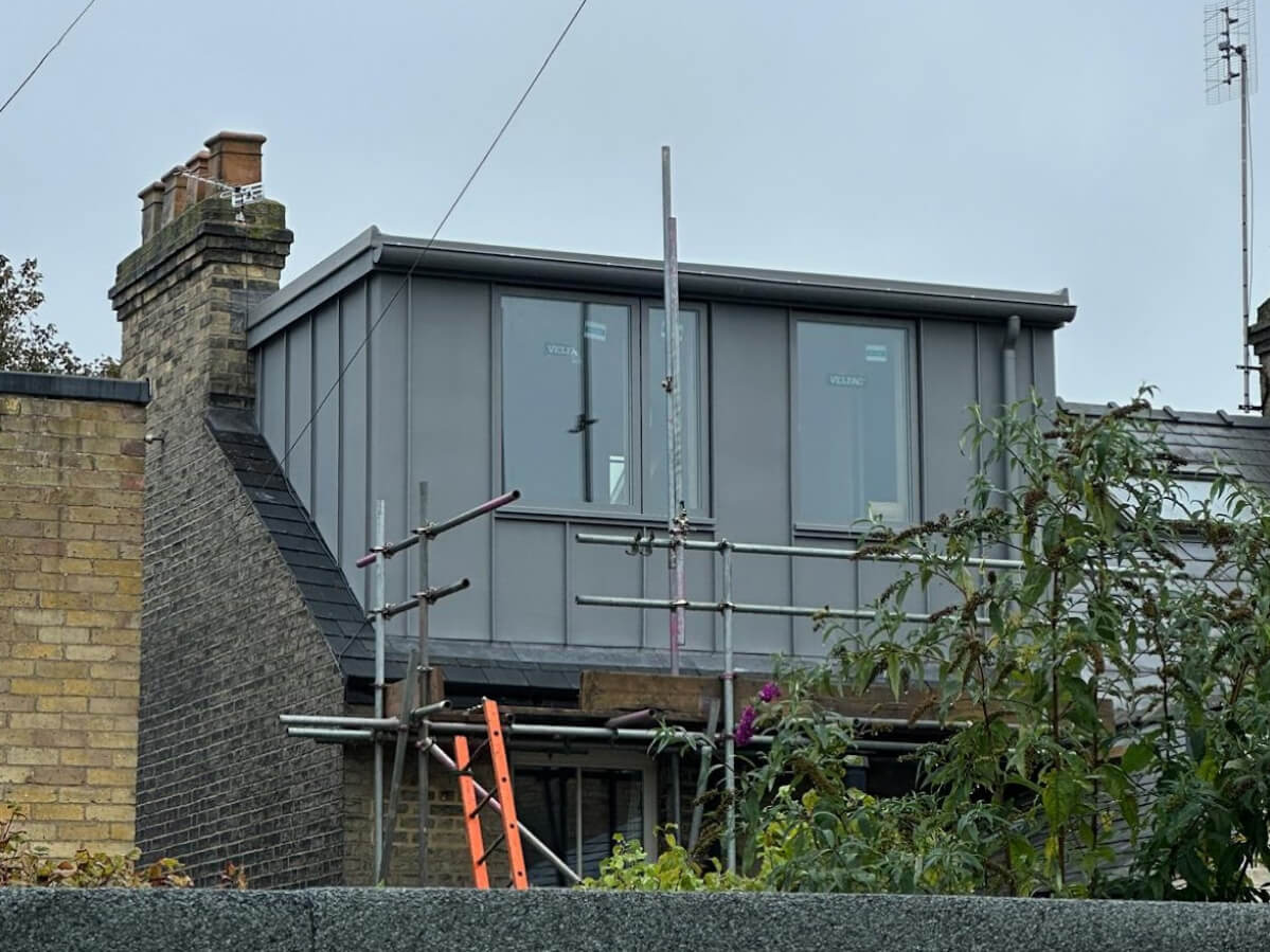 A modern extension with large windows is under construction on top of a brick building, with scaffolding and a ladder visible at the front—perfect for those seeking sash window repair South London expertise.