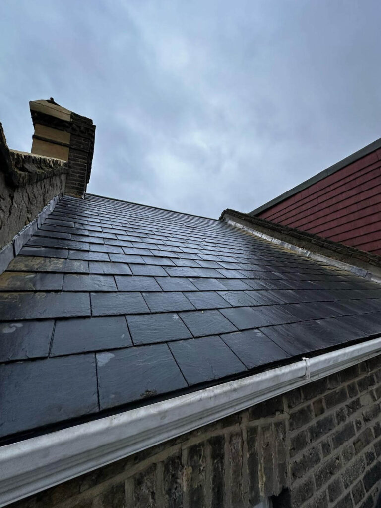 A close-up view of a dark slate roof on a brick building under a cloudy sky.