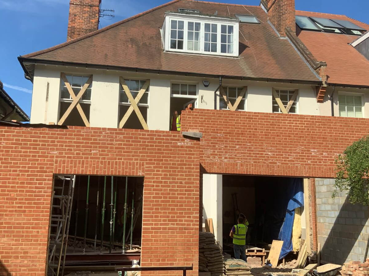 A brick house under renovation with exposed windows, construction materials, and workers visible on the ground and upper floors—ideal for Sash Window Repair South London specialists.