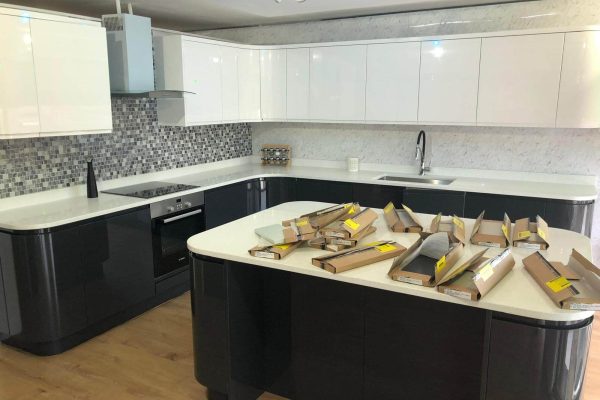 Modern kitchen with black and white cupboards, mosaic splashback, and an island covered with unopened packages and boxes.